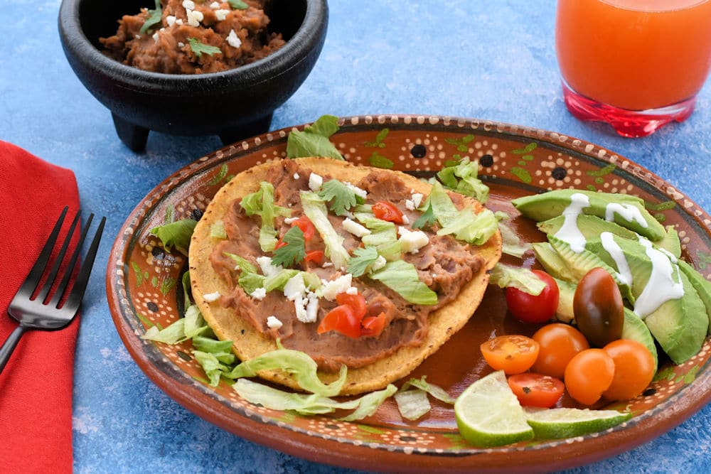 24Bite: Instant Pot Vegan Bean Dip recipe used to make tostadas on a plate with lettuce, tomato and avocado