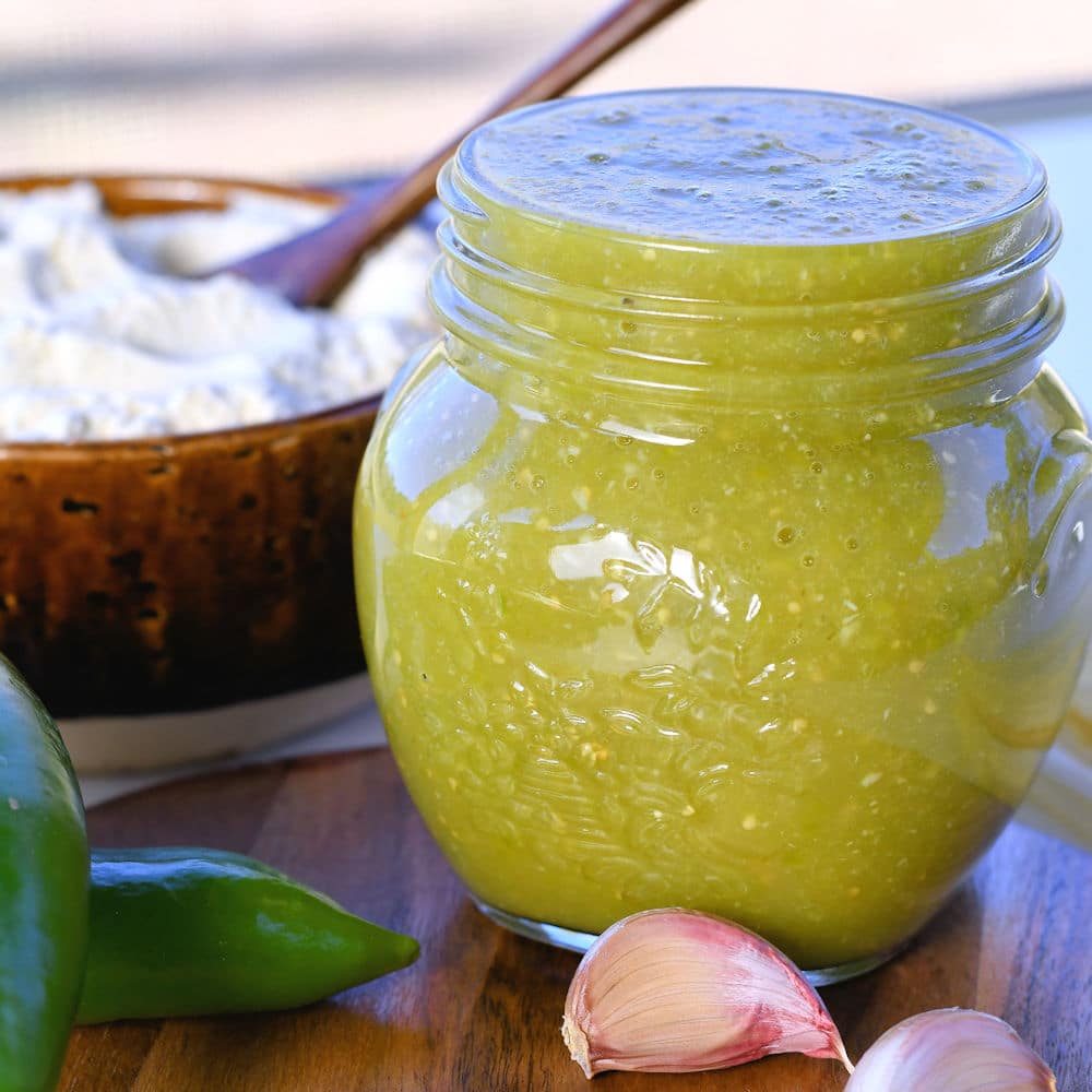 24bite: homemade verde tamale sauce in a jar with anaheim and garlic cloves with a bowl of masa harina in the background