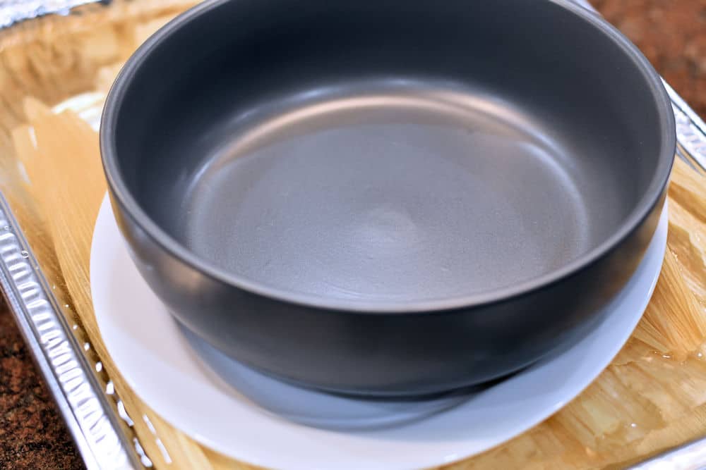 corn husks in water, topped with a heavy bowl to weight them down.