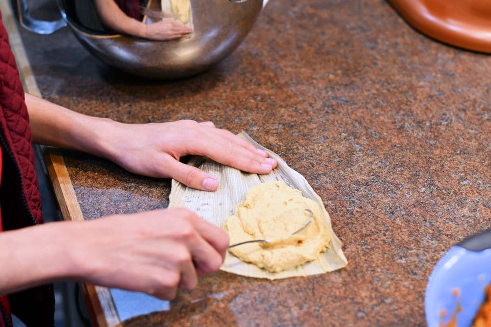 demonstration photo of spreading masa on a corn husk with the back of a spoon
