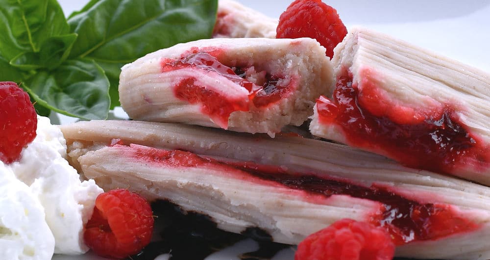 raspberry tamales served with cream and chocolate syrup on a white oval plate.