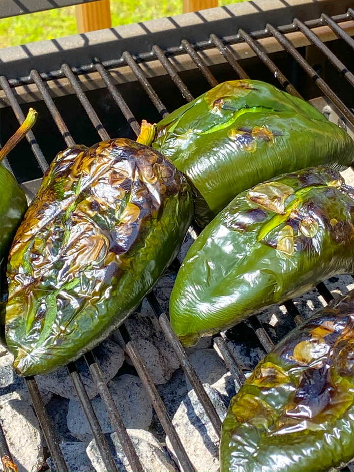 roasting poblano chiles over coals on an outdoor grill