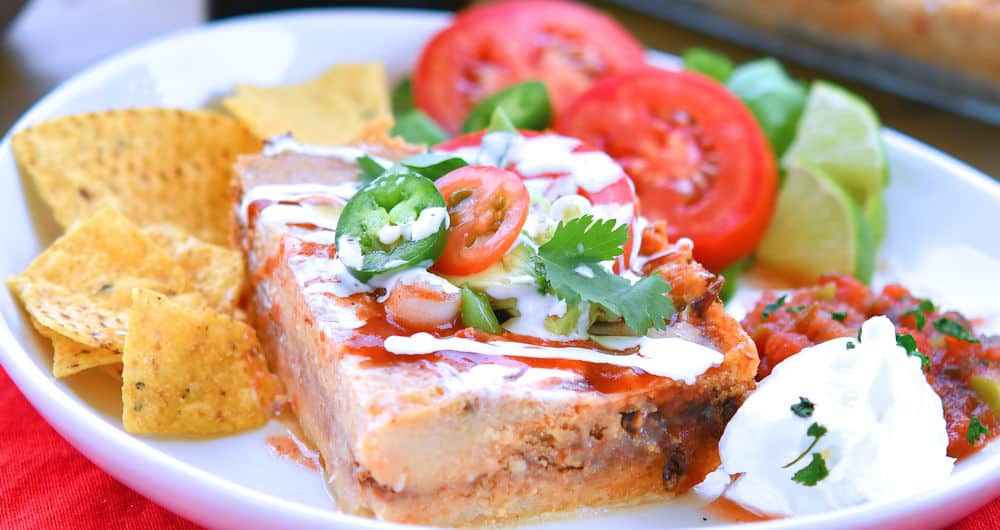 Pork tamale casserole, cut into a square and served with tomato, corn chips and salsa