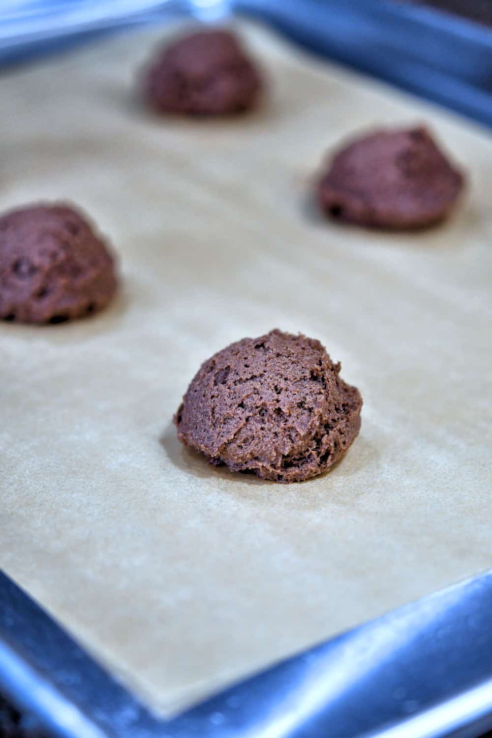 Cookie dough placed on parchment paper on a cookie sheet, ready for baking.