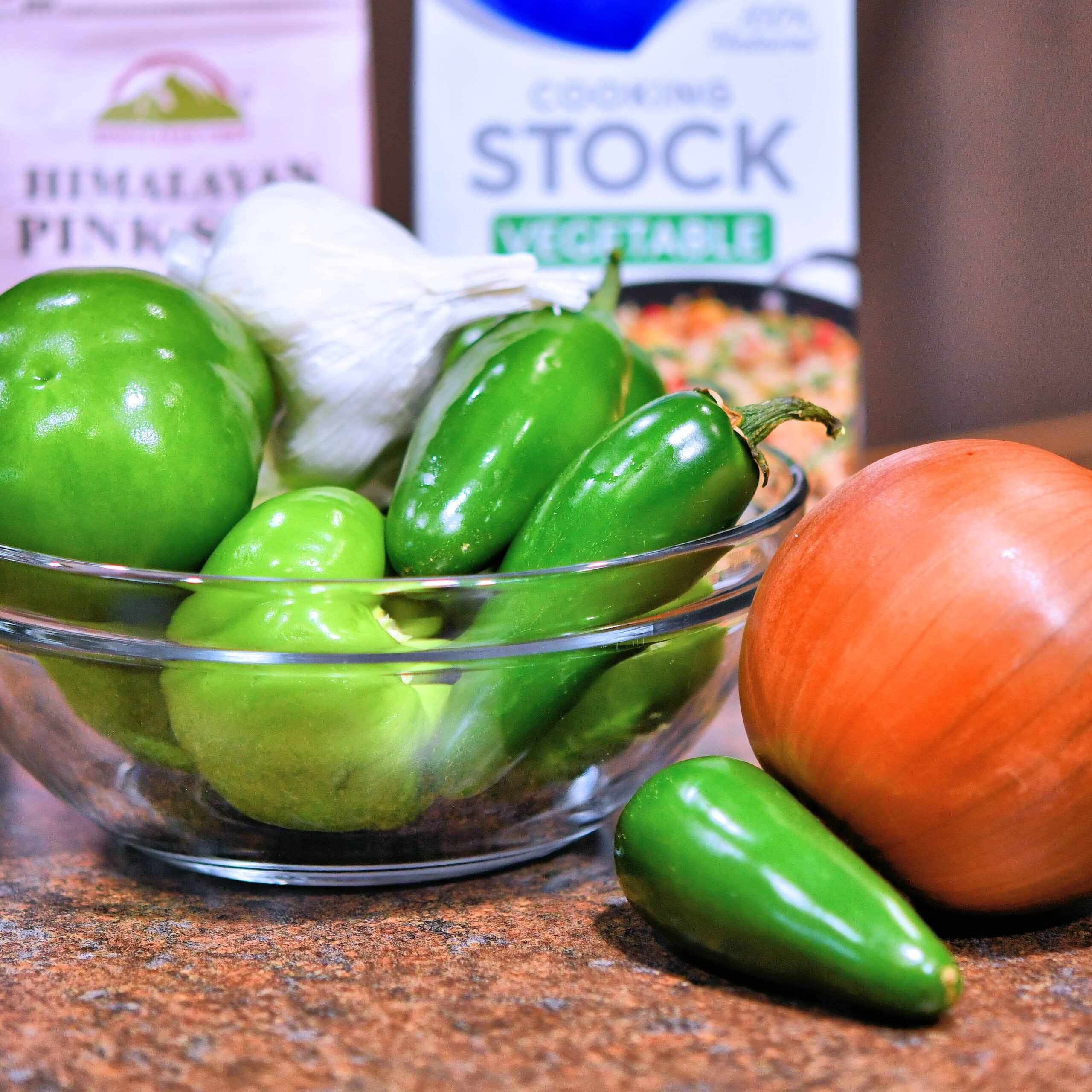 Glass bowl with tomatillos, jalapenos, garlic and onion.