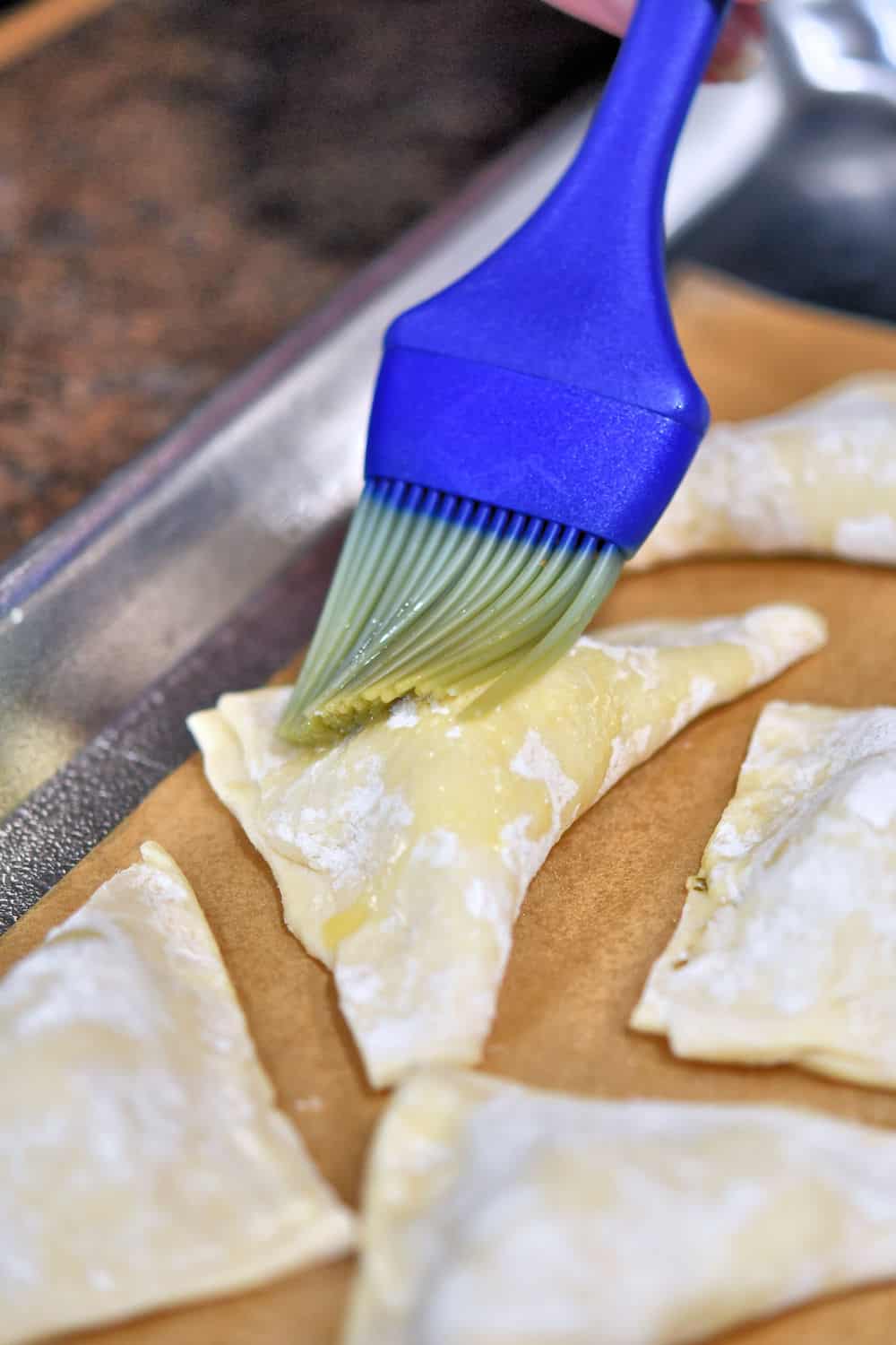 Brush on a little bit of beaten egg on the tops of the puff pastry triangles.