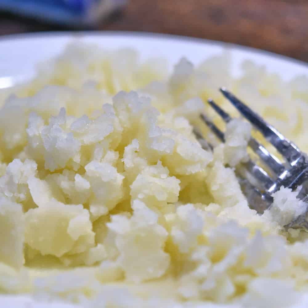 mashing the potato with a fork on a white plate