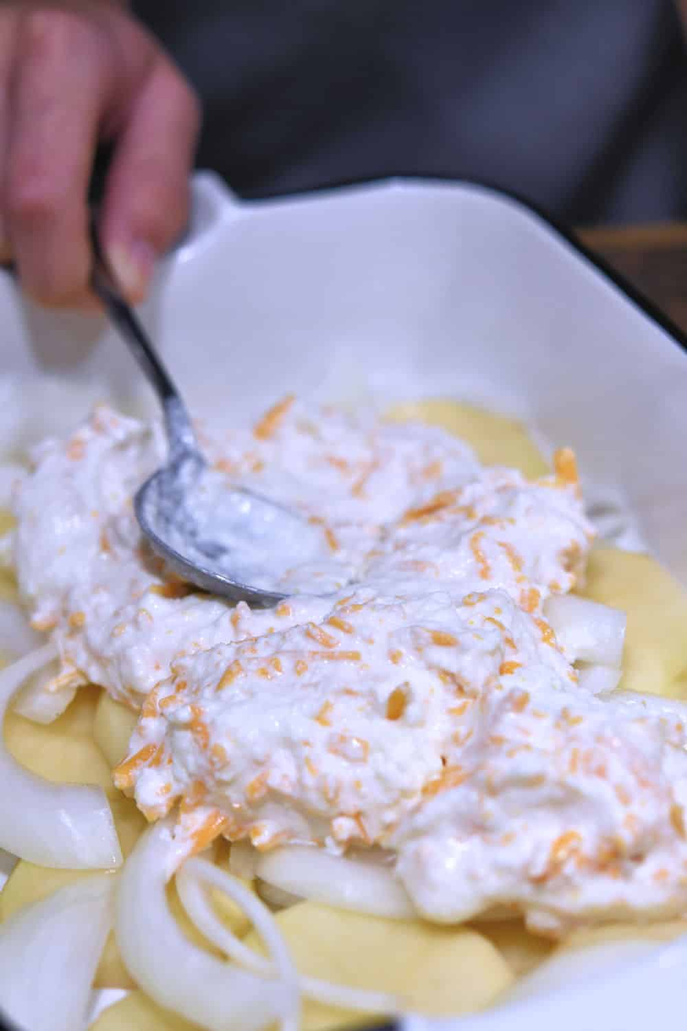 spreading a mixture of ricotta and cheddar cheese on top of sliced potatoes