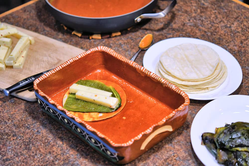 cheese, container of sauce, tortillas and peeled green chiles shown on a counter for assembling cheese enchiladas