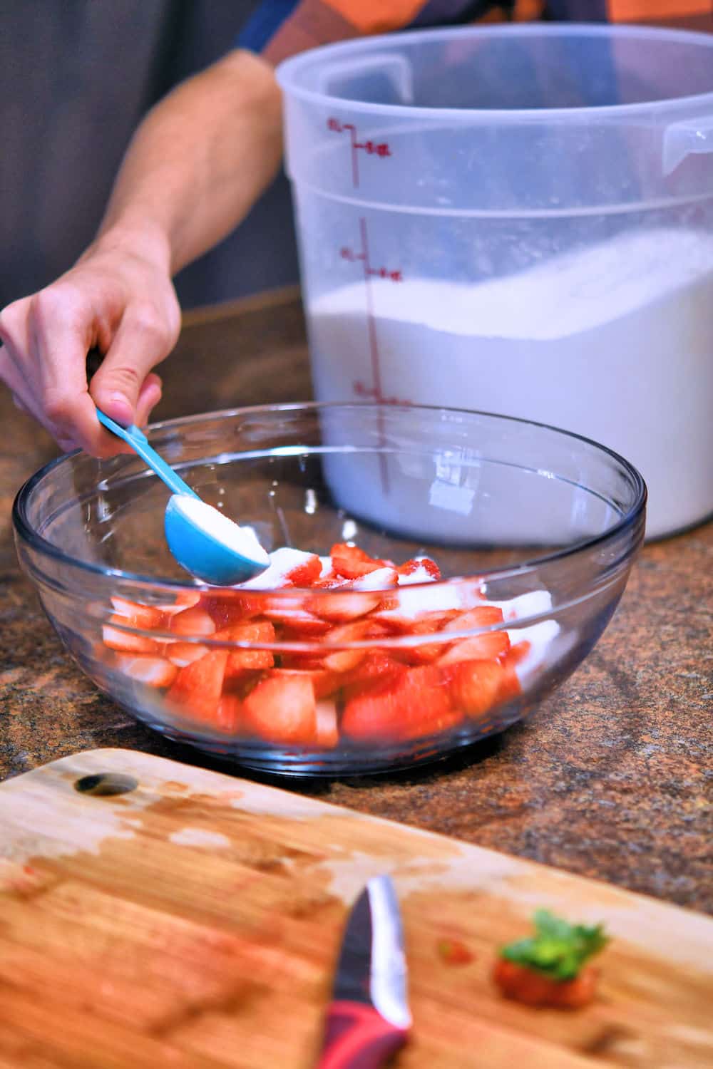 placing sugar in a bowl of fresh sliced strawberries to macerate