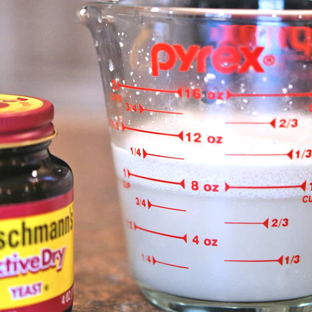 glass measuring cup with water and yeast, starting to foam in proofing the yeast