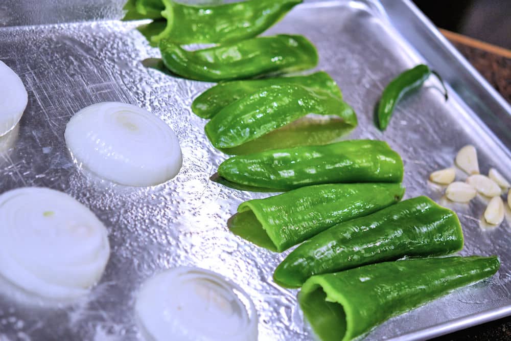 sliced onions, halved Anaheim chile peppers and garlic cloves on a cooking sheet, ready for the broiler oven.