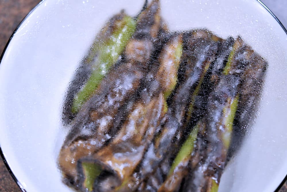 roasted chile peppers in a bowl covered with plastic wrap