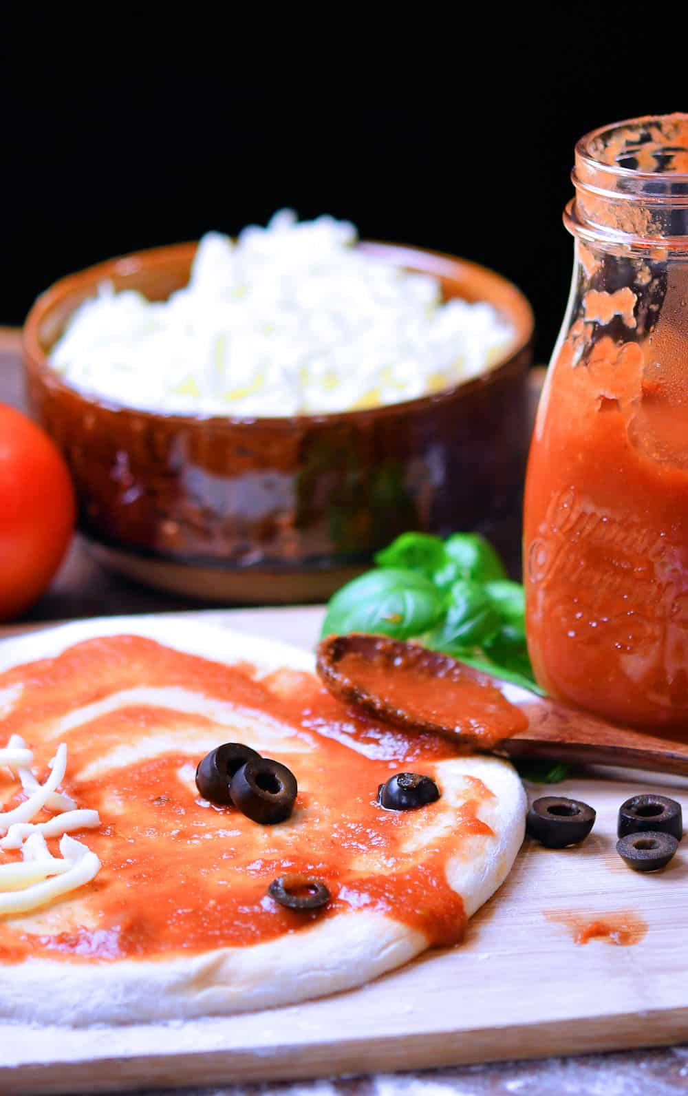 fresh rolled pizza dough on a cutting board with a spoonful of tomato sauce