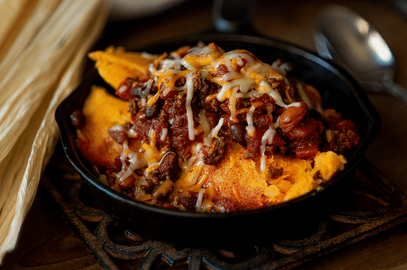 Beef short rib tamales in a black bowl sved with beans and melted cheese.