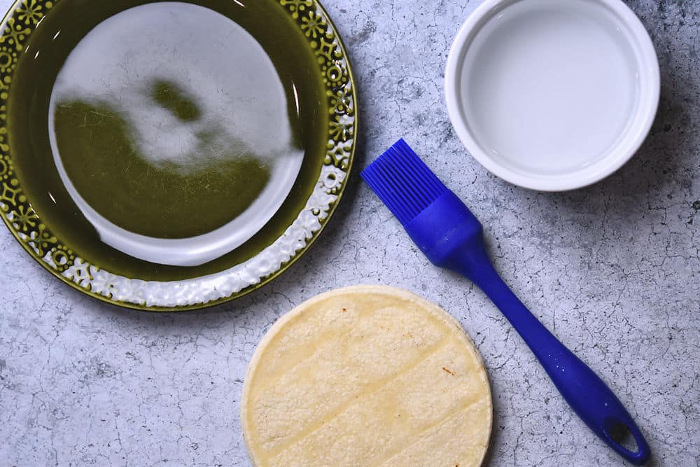 plate, bowl of water and pastry brush on a counterop to soften corn tortillas