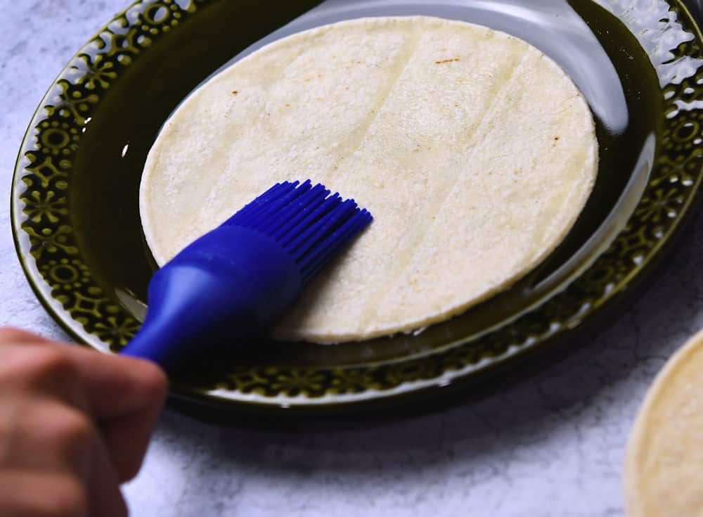 using a pastry brush to add water to a corn tortilla for softening