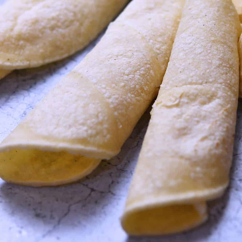 Heated corn tortillas, rolled easily without breaking, displayed on a granite counter.