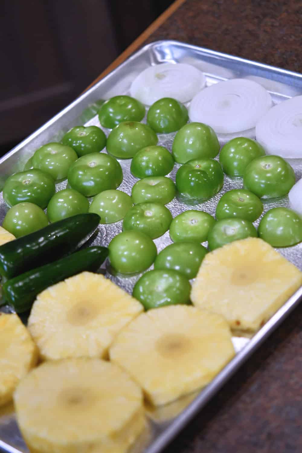 sliced pineapple, tomatillos and jalapenos on a baking sheet, ready for broiler