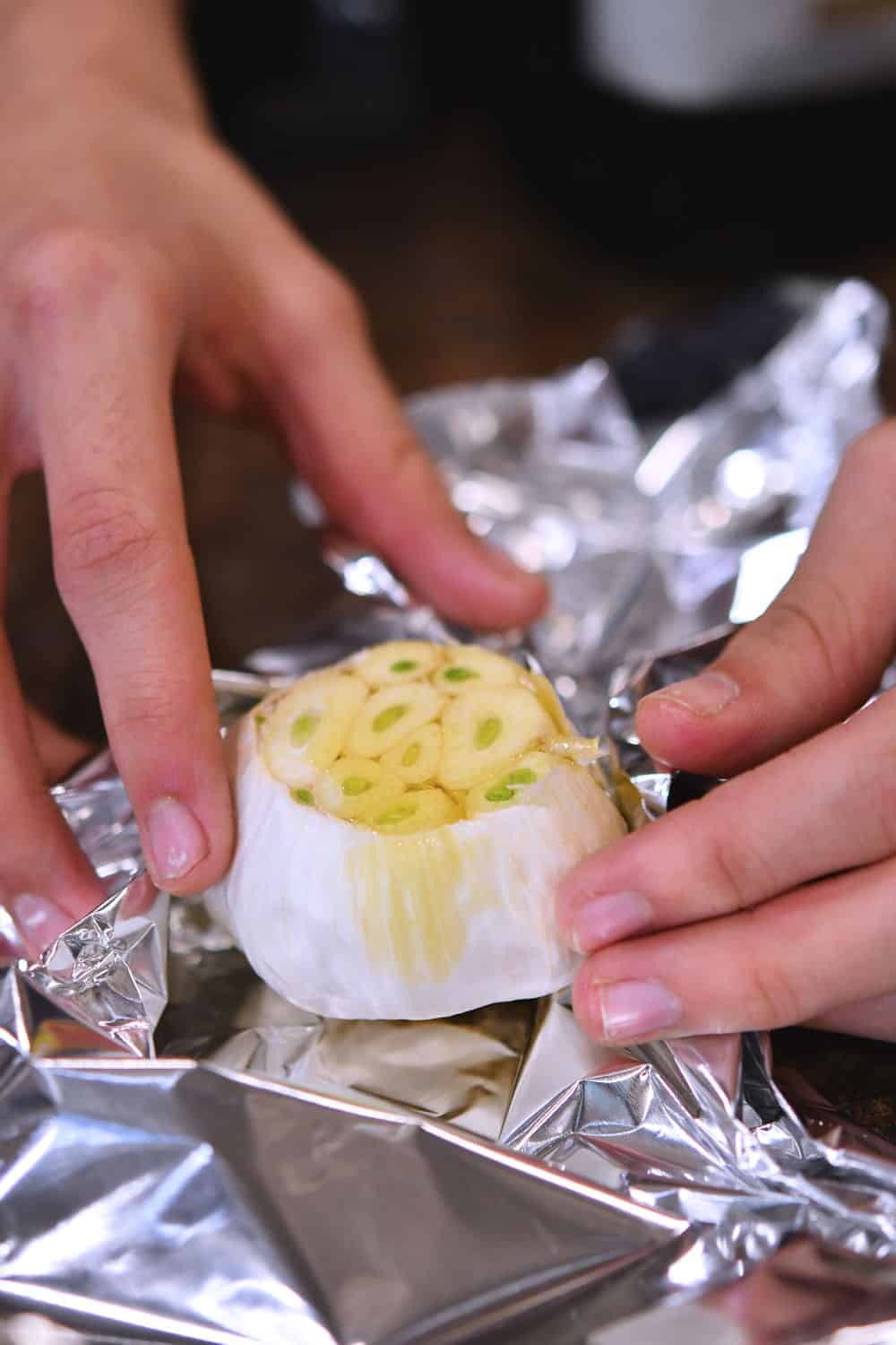 wrapping a head of garlic in foil to prepare it for roasting