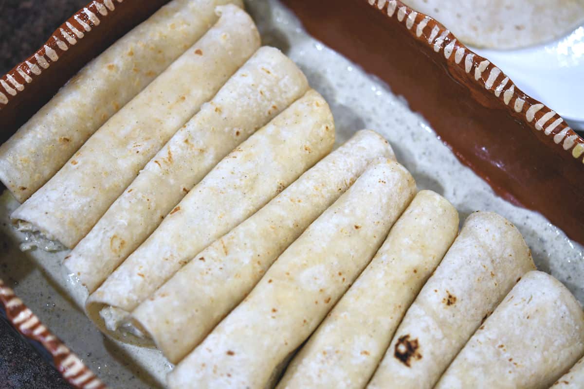 Baking pan with rolled tortillas, ready for topping and cheese