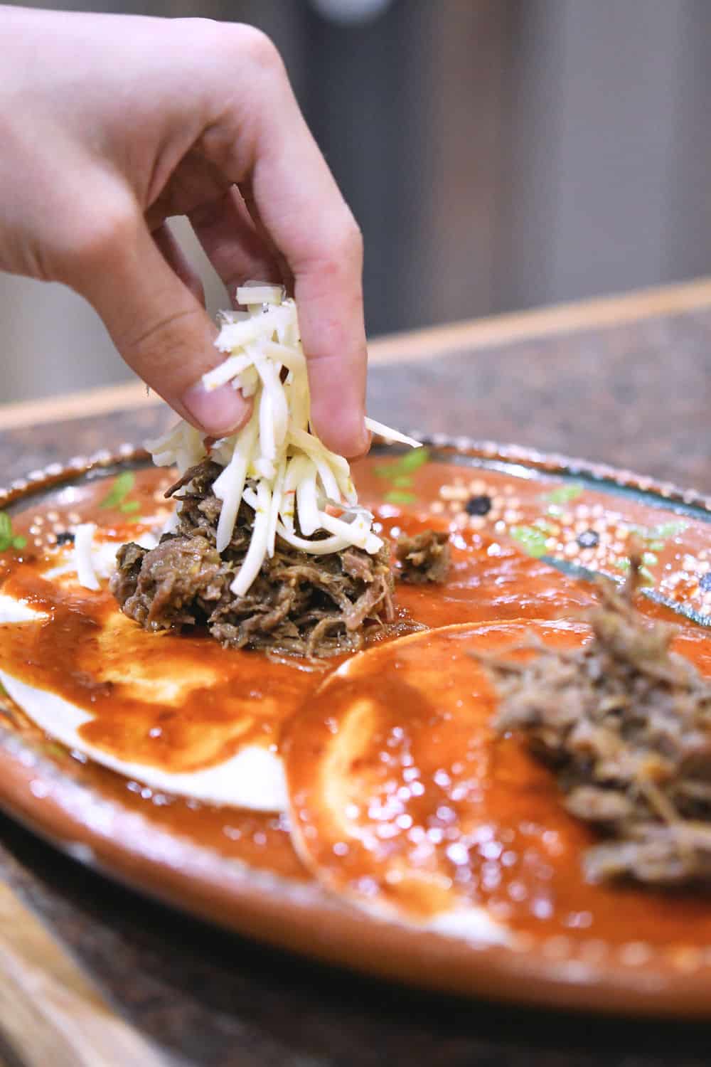 Two beef enchiladas being filled with shredded beef and cheese.