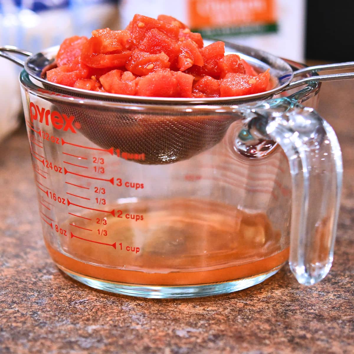 a glass measuring cup with caned tomatoes draining from a mesh strainer