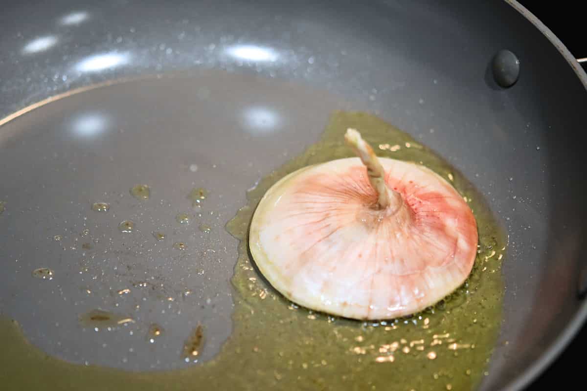 The top of an onion being sauteed in olive oil, cut side down.