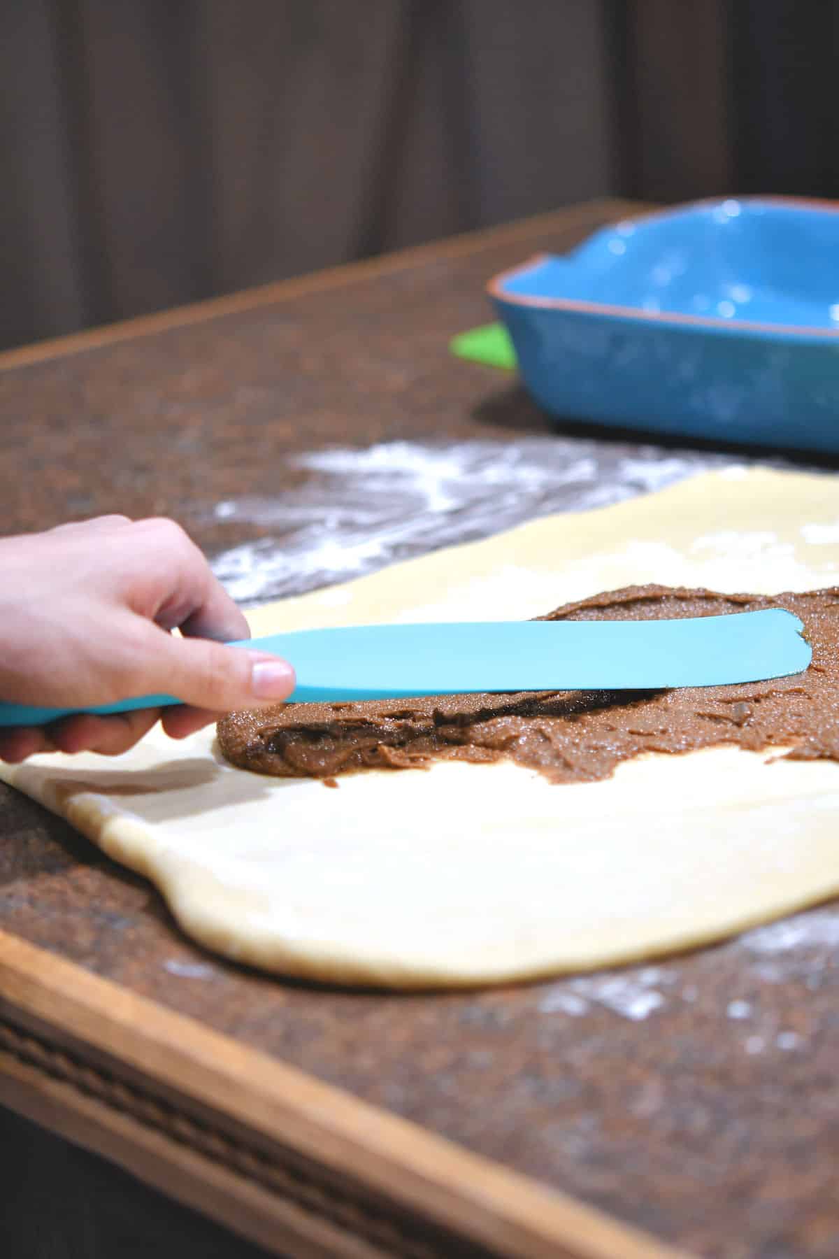 using a spurtle to spread cinnamon mixture on rolled out dough