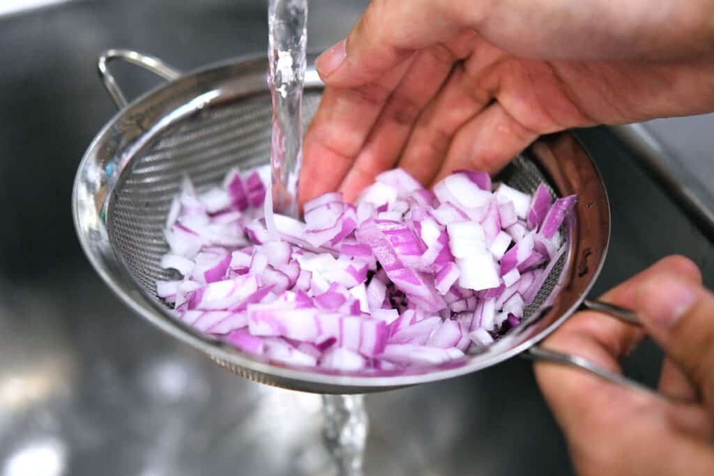 running water over chopped red onion in a colander