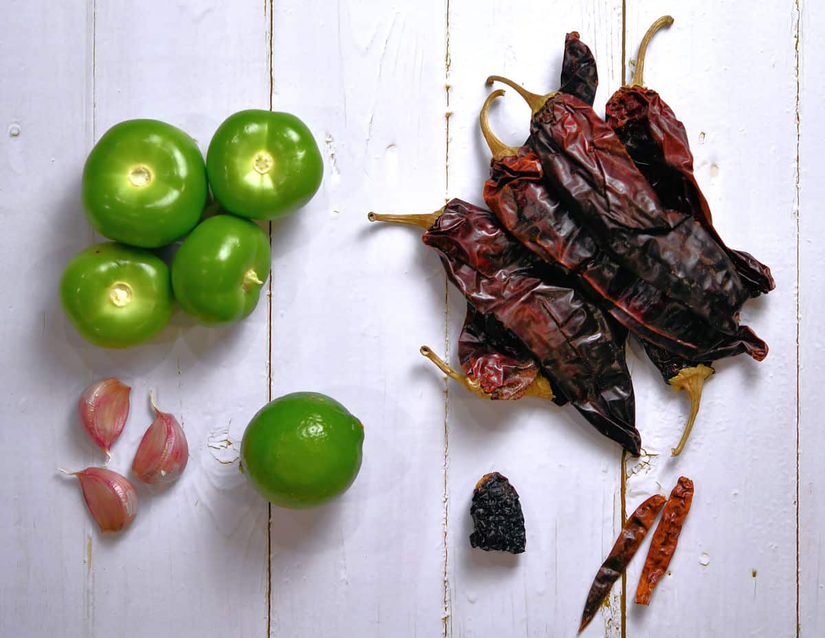 tomatillos, garlic, lime and red chiles on a white wooden table