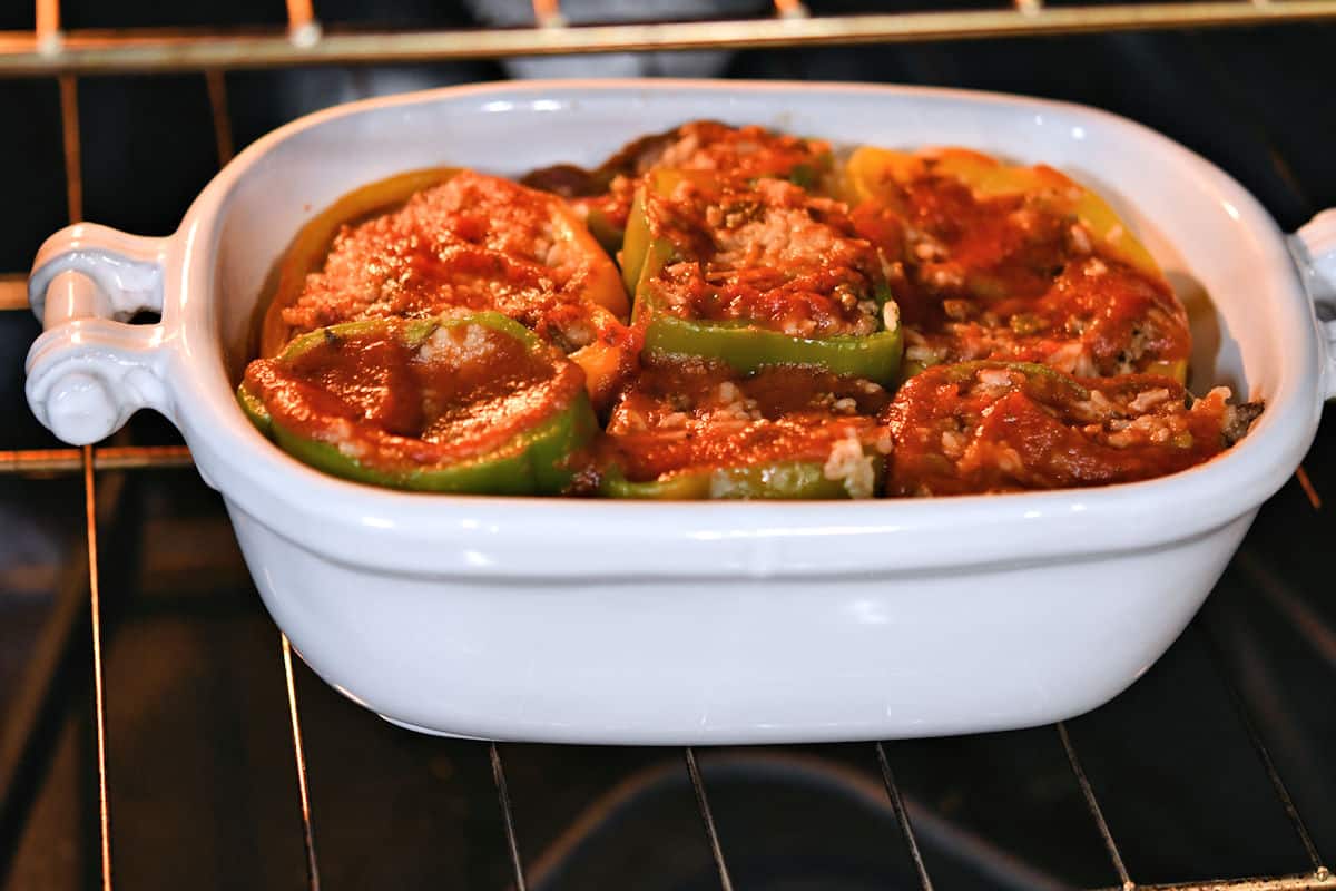 a deep dish oval ceramic baking dish with stuffed bell peppers, inside an oven