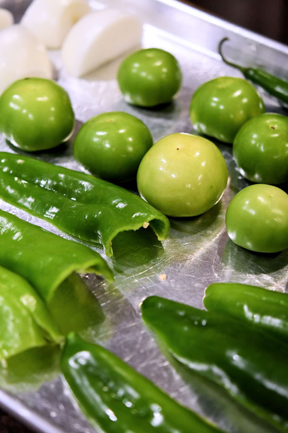 Anaheim chiles and tomatillos on a baking sheet, ready for broiling in the oven