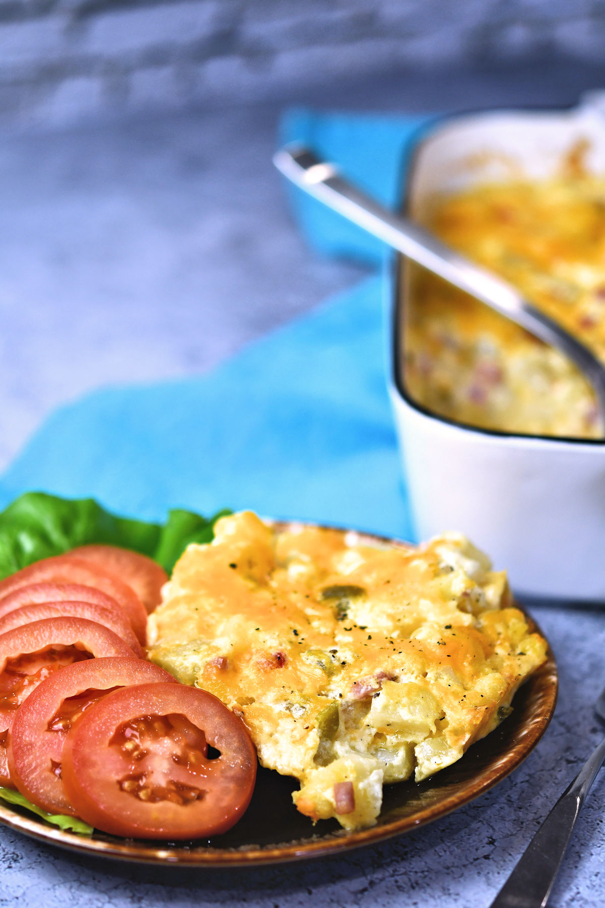 A serving of potato breakfast casserole, on a plate, served with sliced tomatoes.