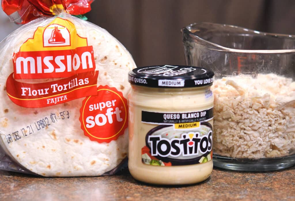 ingredients of flour tortillas, queso and chicken on a countertop