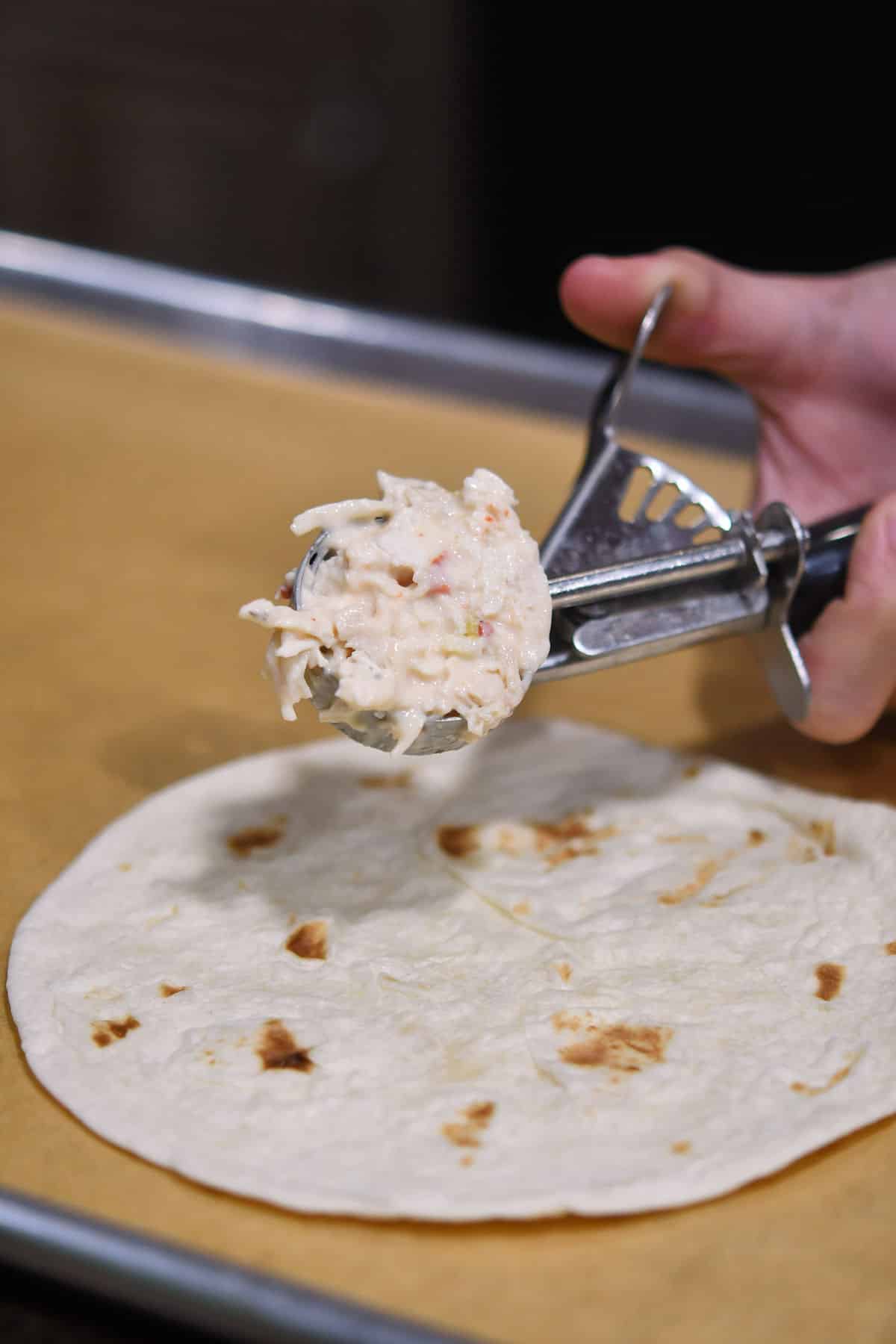 A cookie scoop with an even amount of chicken filling ready to be placed in tortilla