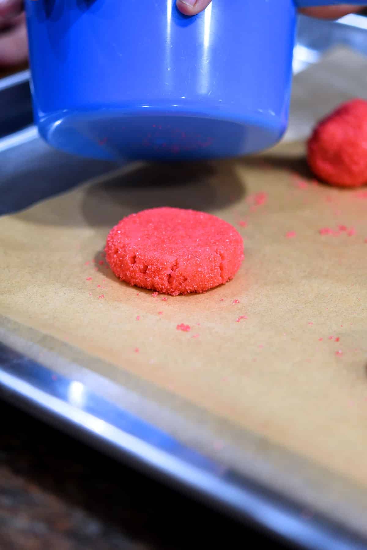 a ball of cookie dough being flattened with a measuring cup