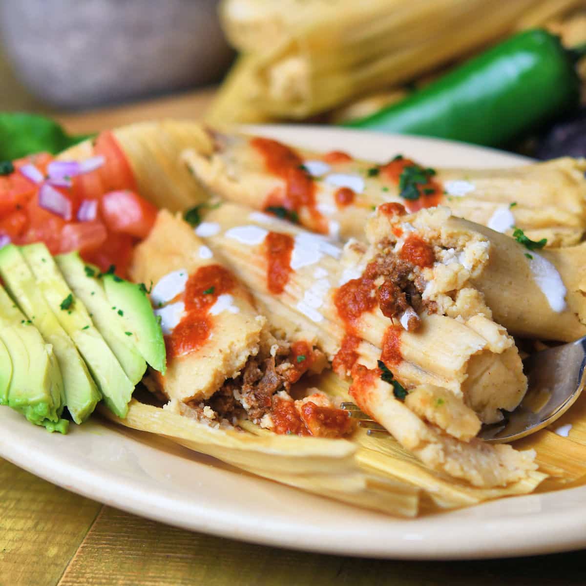 pork tamales on an oval plate with avocado and tomato salsa