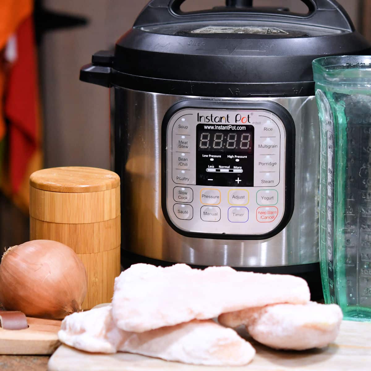frozen chicken breasts, onion on a countertop in front of an Instant Pot pressure cooker