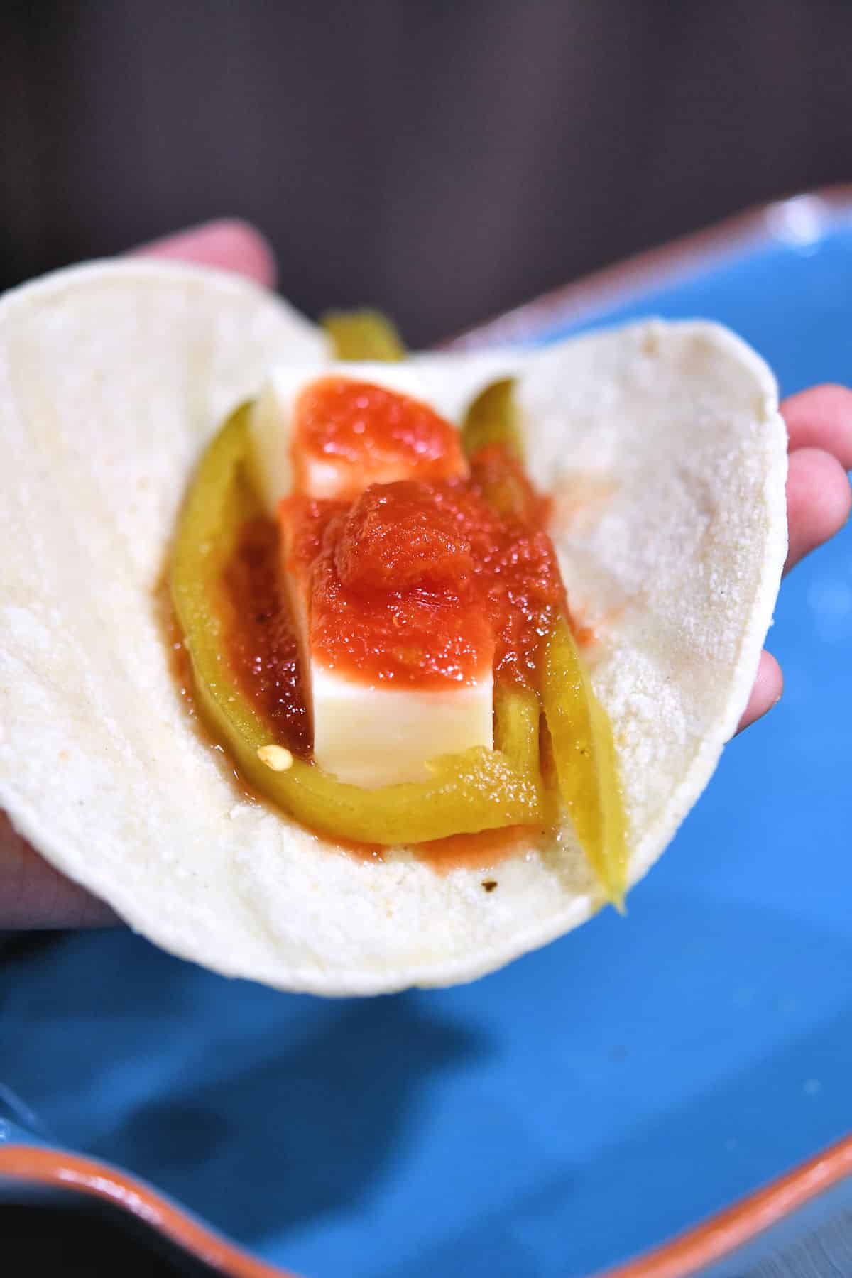 closeup of filling corn tortilla with monterey jack cheese and strips of green chiles and tomato