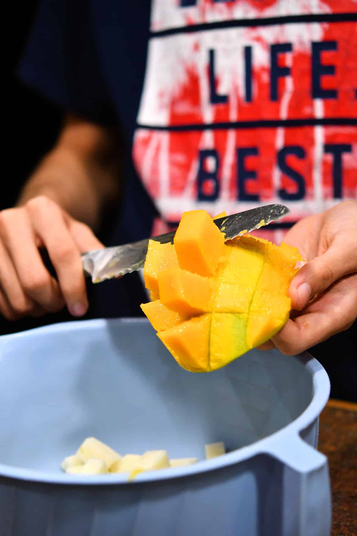 cutting cubes of mango from the skin into a bowl