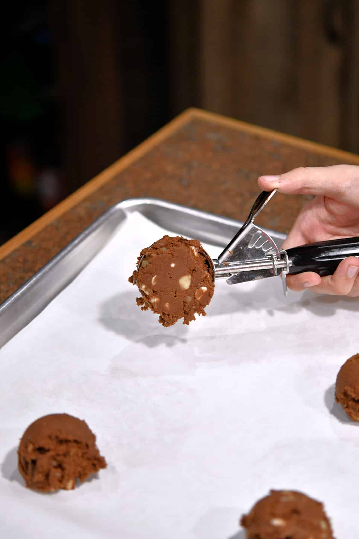 scooping chocolate cookie dough onto white parchment paper
