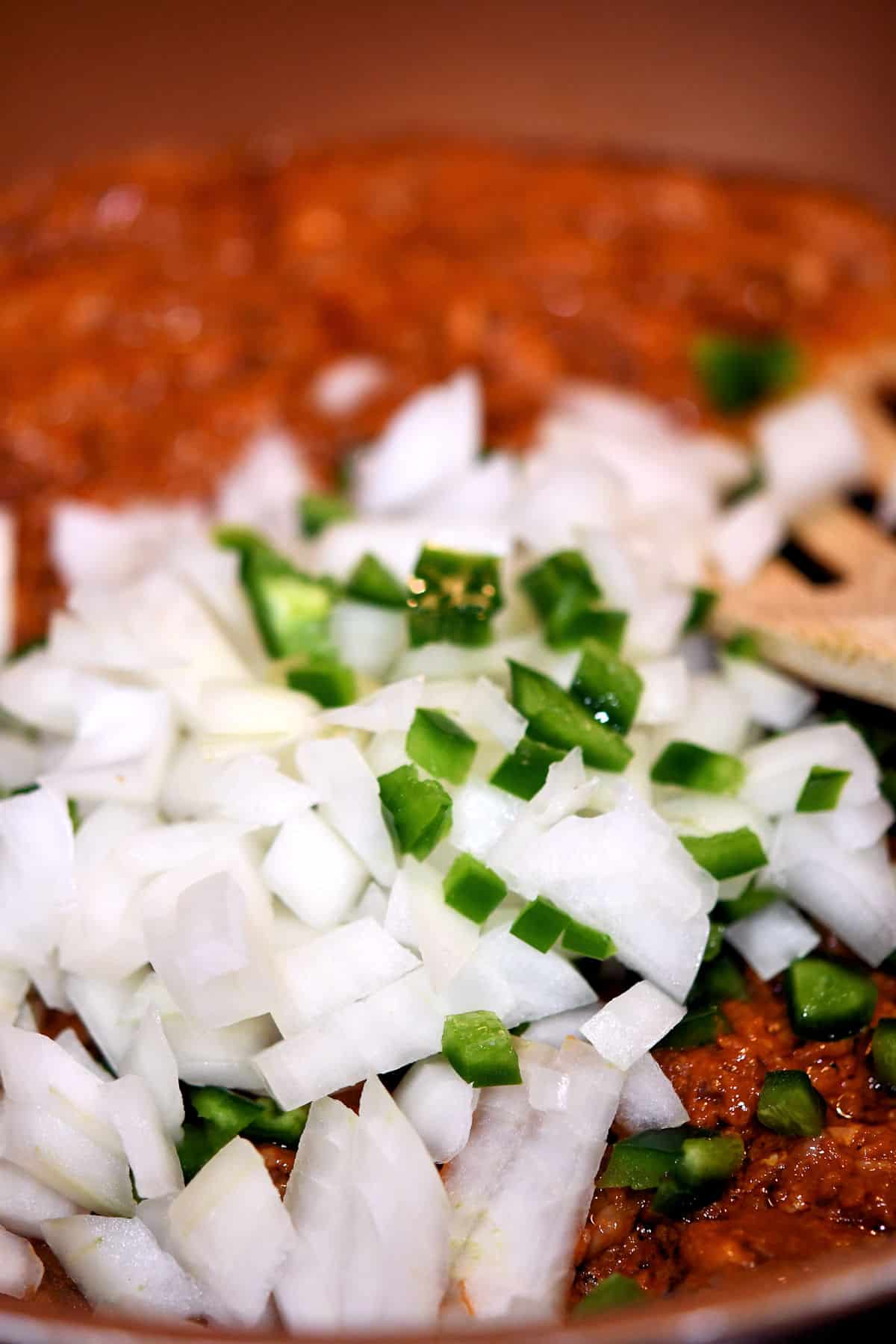 close up of skillet with uncooked onions and bits of jalapeno