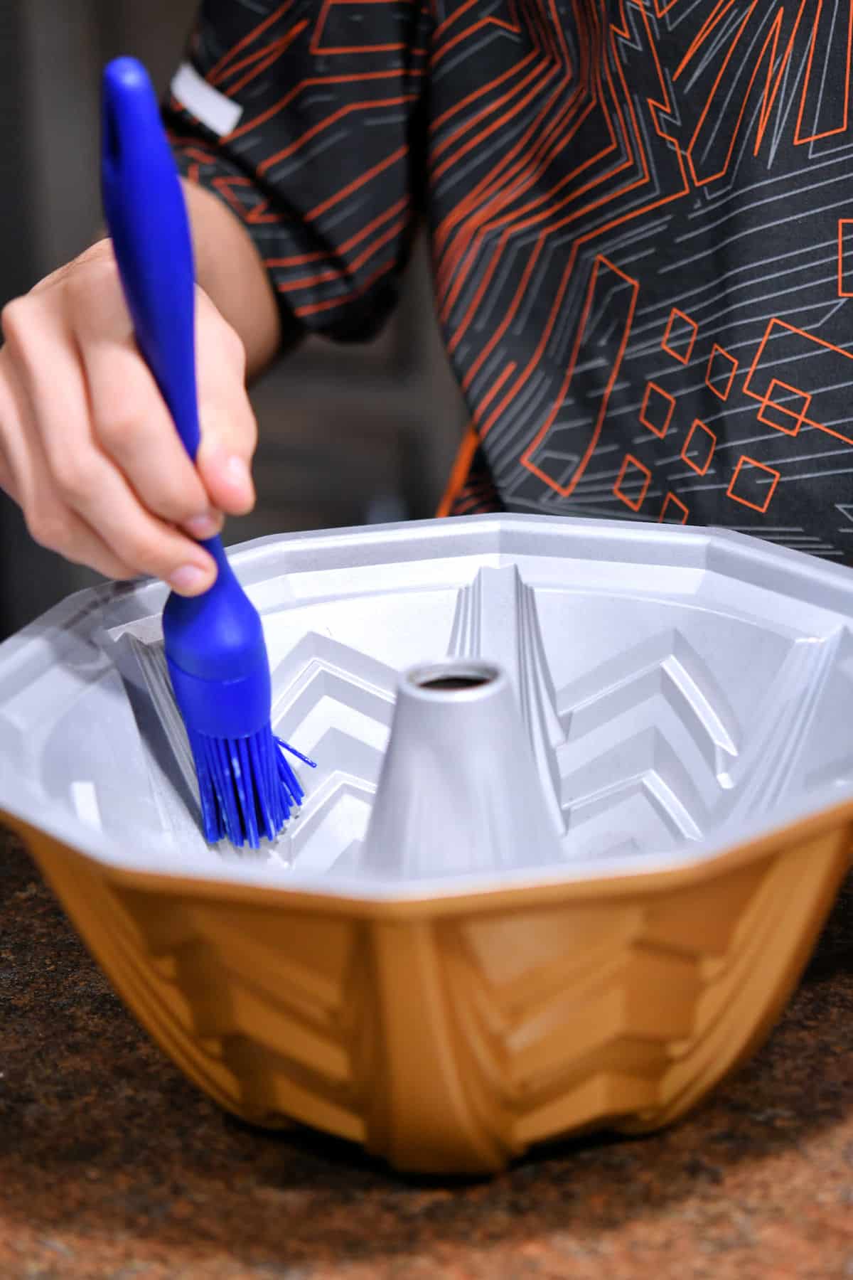 using a silicone brush to push the baking spray into the spaces of the marquee bundt pan