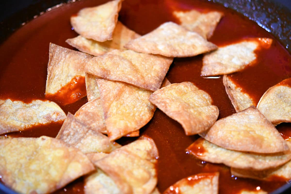 Baked chips, simmering in red sauce for chilaquiles