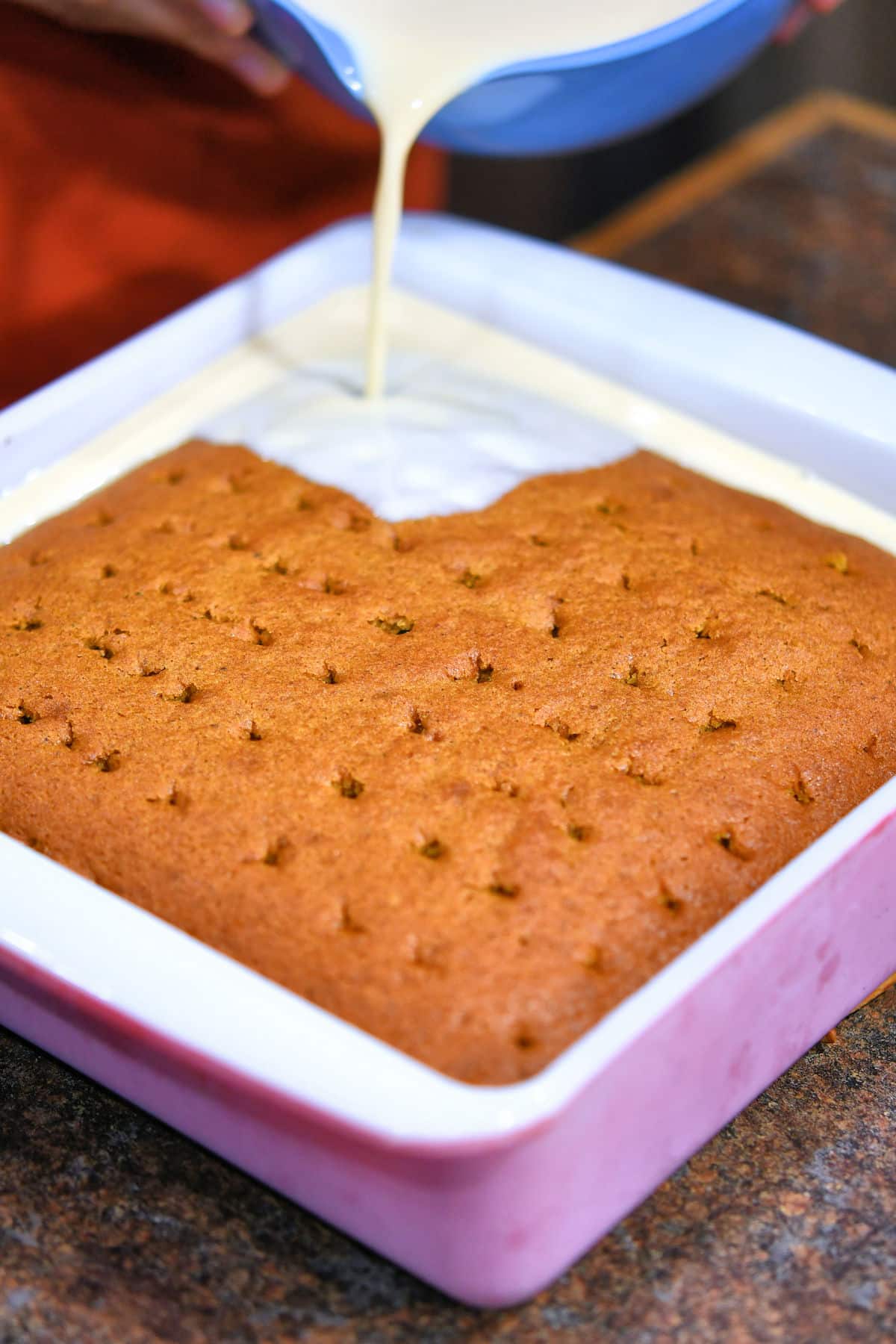 closeup of pouring milk mixture over warm cake