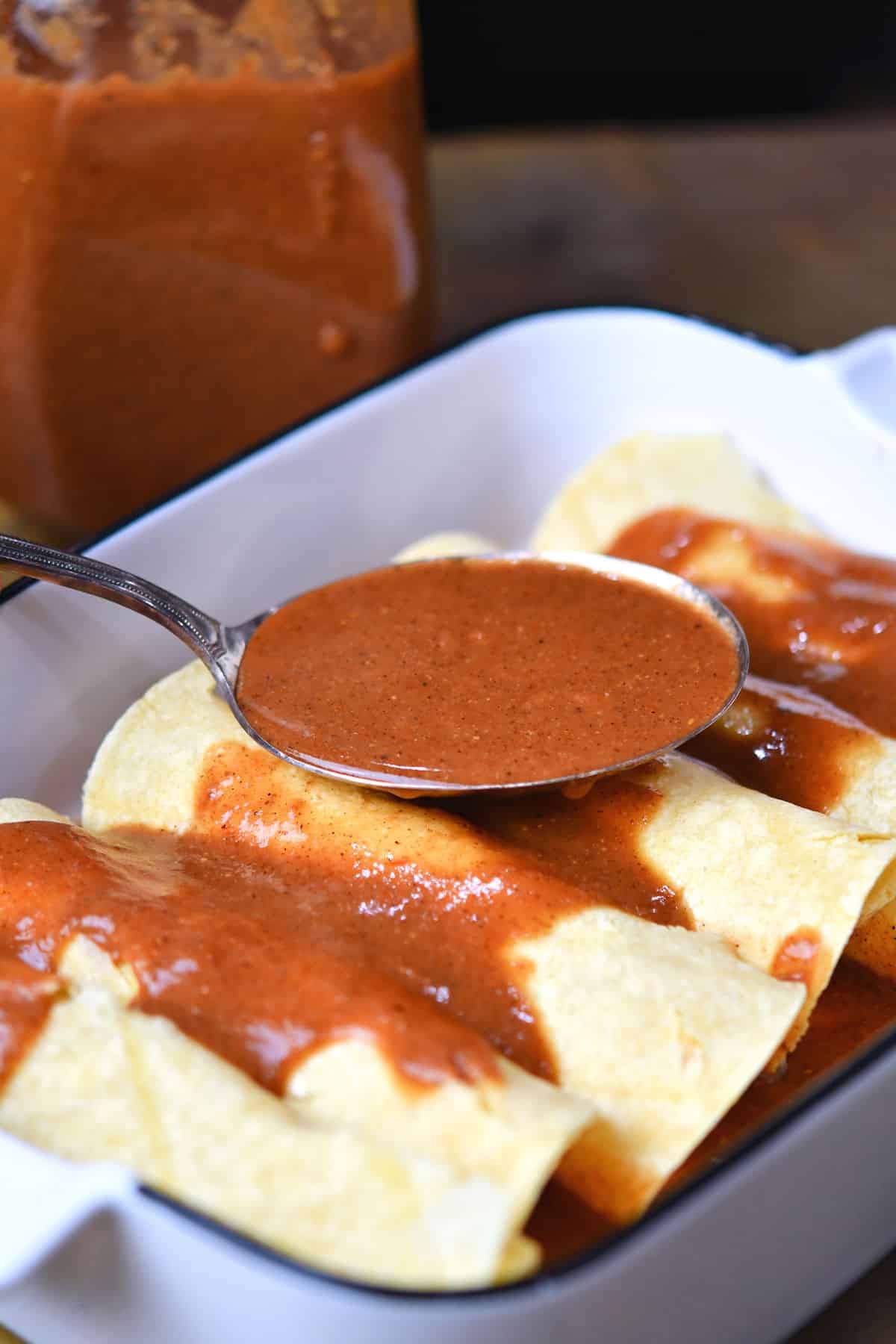closeup of spooning enchilada sauce over rolled tortillas
