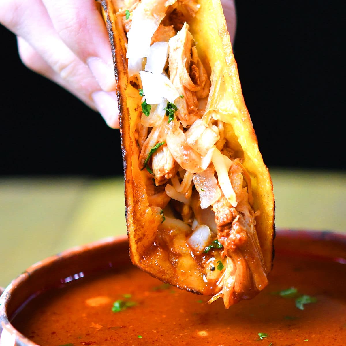 closeup of chicken birria taco being dipped into bowl of sauce