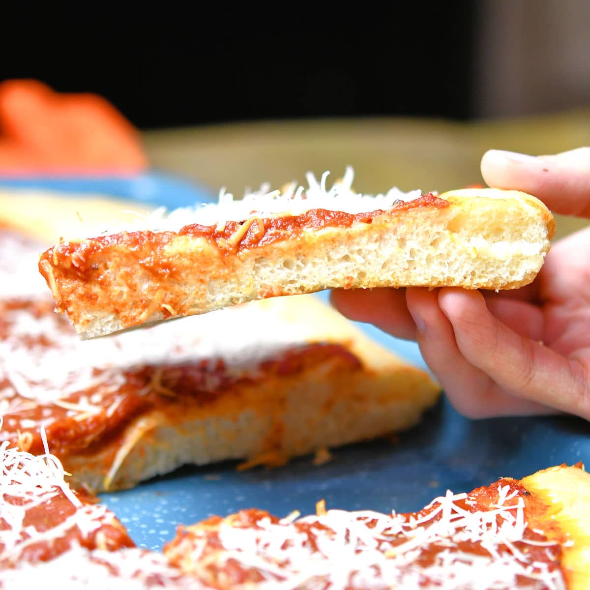 a hand holding a slice of tomato pie horizontally to show the thickness of the crust