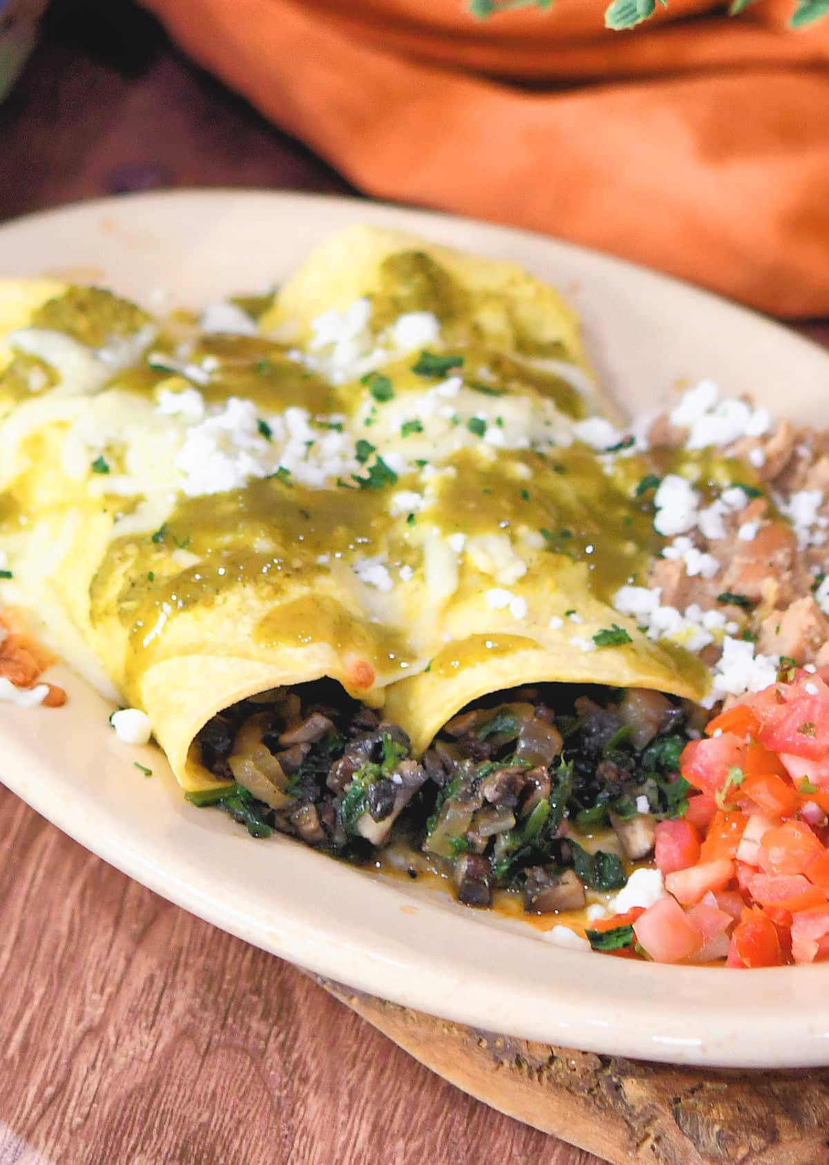 veggie enchiladas on an oval plate, covered in green salsa verde and queso fresco